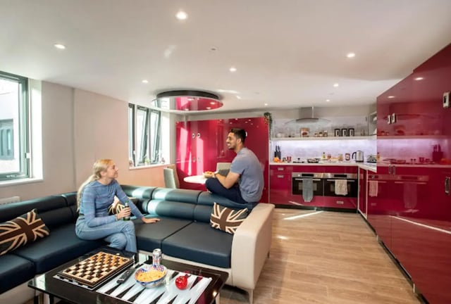 Two people relaxing on sofa next to red kitchen living room at Reynard House in Leicester Student Accommodation