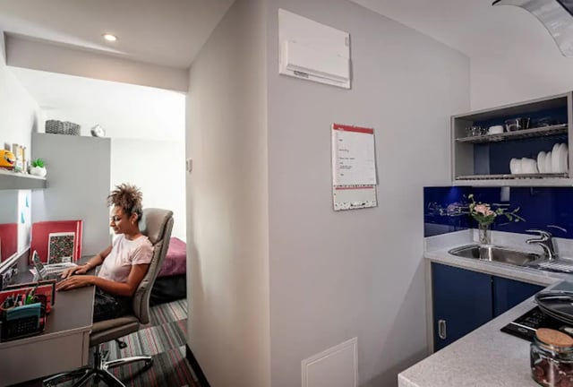 Student working at desk in bedroom and kitchen area at Study Inn Loughborough - Lemyngton Street in Loughborough Student Accommodation