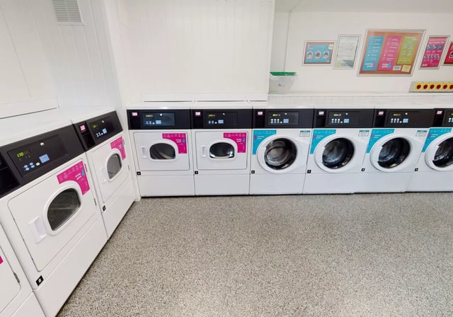 Washing machines and dryers arranged in a row laundry room at iQ Century Square in Sheffield Student Accommodation