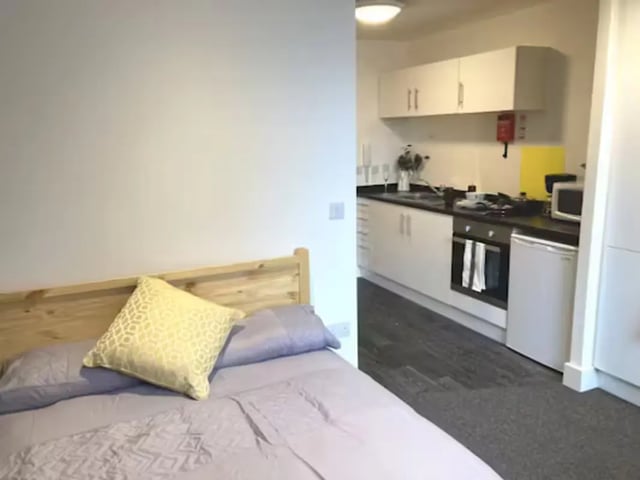 Bed with yellow pillow and kitchen area bedroom kitchen at Hydrogen in Nottingham Student Accommodation