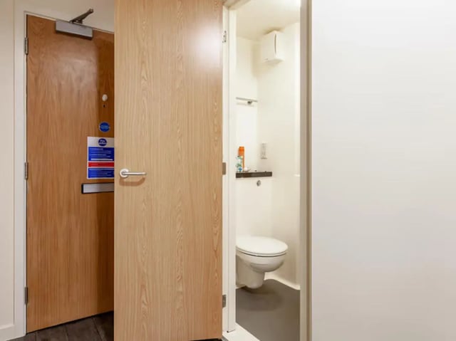 Toilet with shelf and toiletries inside bathroom at Neuadd Kyffin in Bangor Student Accommodation