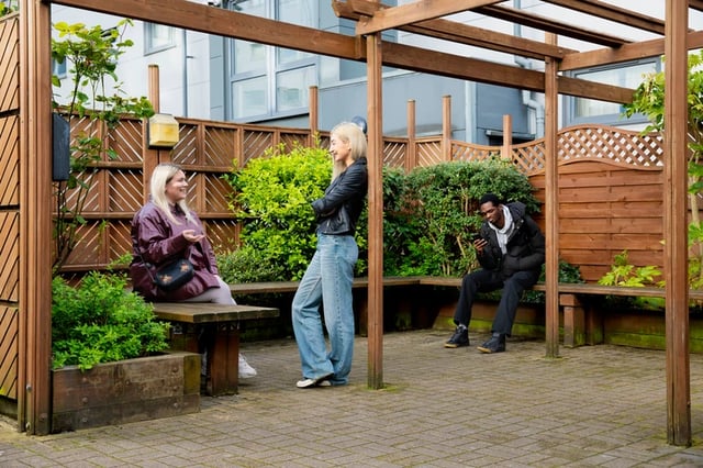 People relaxing on wooden benches in courtyard exterior at Liberty Park in Leicester Student Accommodation