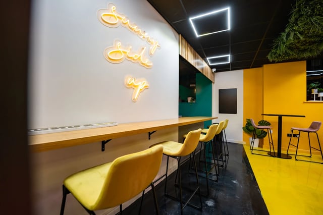 Neon sign yellow bar stools black table dining area at Urban Hub in Preston Student Accommodation