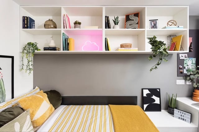Bed with yellow blanket shelves with books bedroom at Artisan Heights in Manchester Student Accommodation