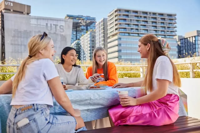 Four students sit around a table outdoors living room exterior at Broadway x Scape in Sydney Student Accommodation