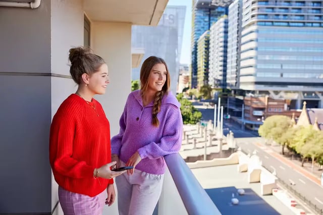 Two students on balcony overlooking city exterior at Broadway x Scape in Sydney Student Accommodation