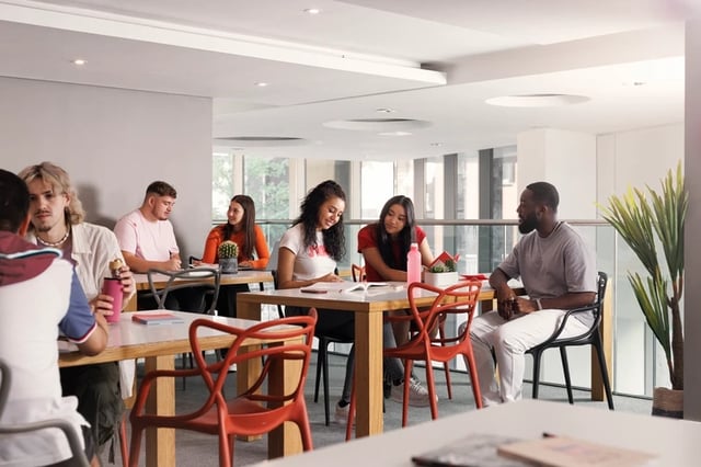 Students studying at communal tables with red chairs communal area at Bridgewater Heights in Manchester Student Accommodation
