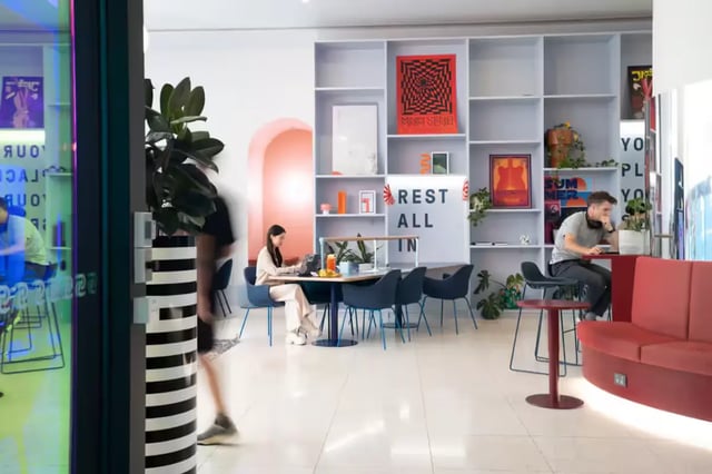 People working at tables with red sofa lounge at Scape Aurora in Melbourne Student Accommodation
