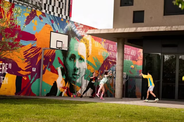 Students playing basketball by colourful mural exterior at Scape Waymouth in Adelaide Student Accommodation