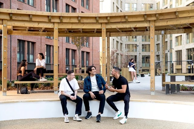 Students relaxing on benches under wooden structure outdoor area at Morriss House in Nottingham Student Accommodation