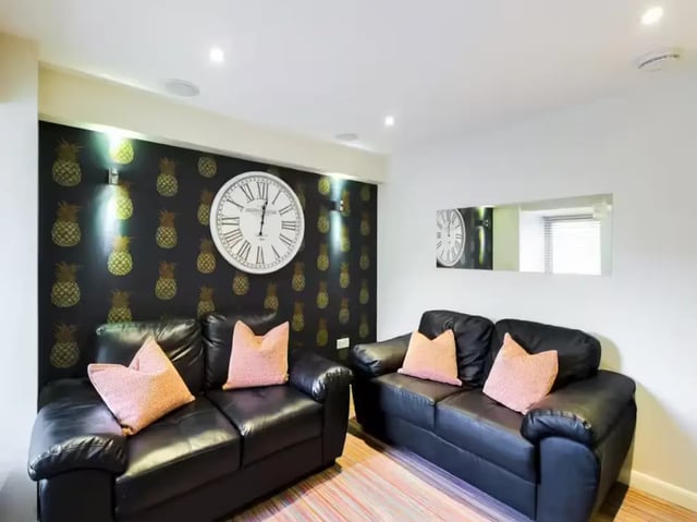 Two black sofas pineapple wallpaper large clock living room at 2 Queen Anne Street in Stoke-On-Trent Student Accommodation