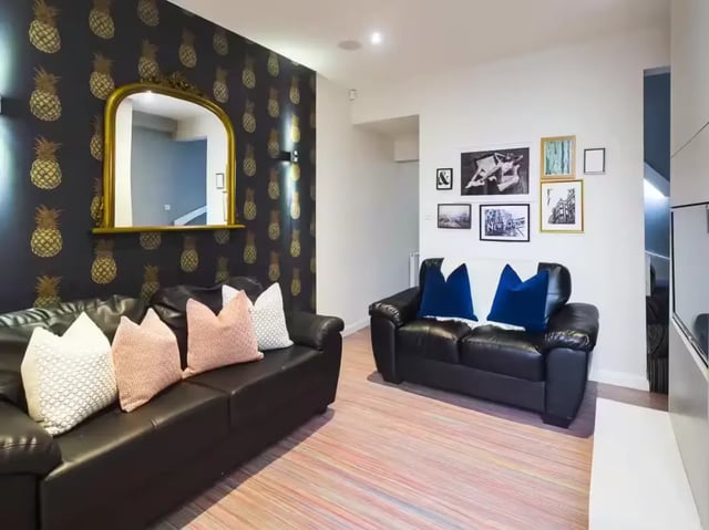Two black sofas pineapple wallpaper mirror living room at 48 Cauldon Road in Stoke-On-Trent Student Accommodation