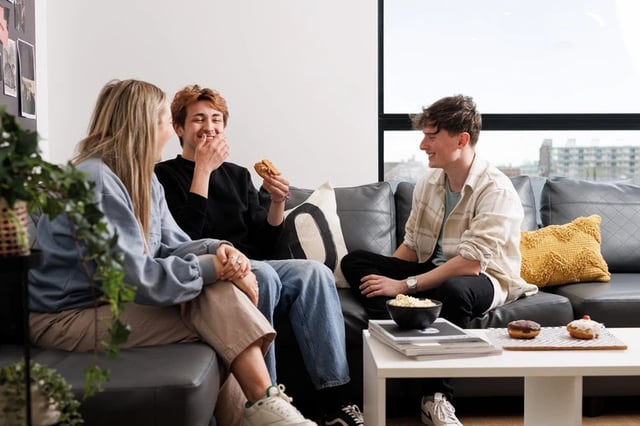 Students relax on sofa with snacks living room at Chaucer House in Portsmouth Student Accommodation