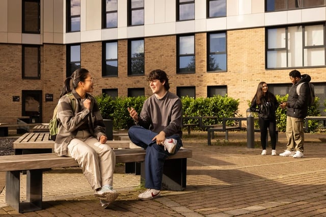 Students talking on benches outside accommodation exterior at Brass Founders in Sheffield Student Accommodation