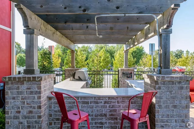Grill and red chairs under pergola exterior at Champions' Club in Fayetteville Student Accommodation