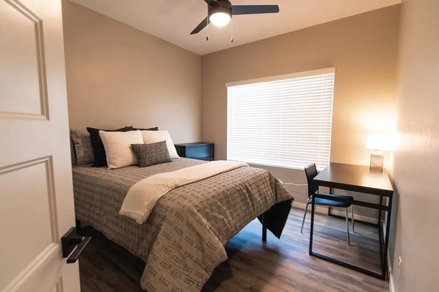 Bed with pillows bedside table desk lamp chair bedroom at Lofts on 8th in Tempe Student Accommodation