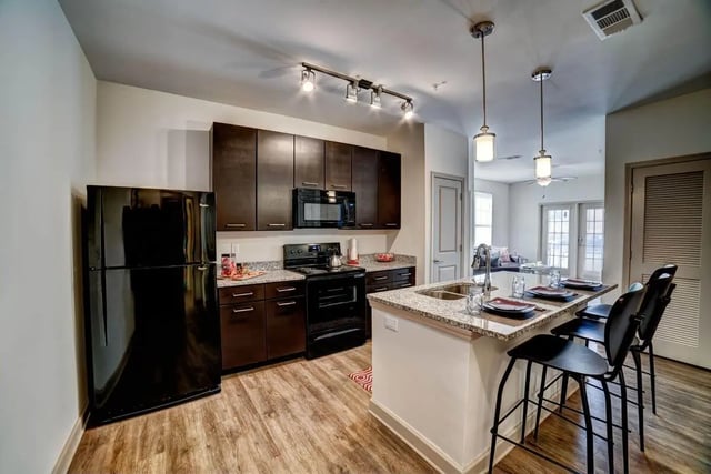 Black refrigerator dark cabinets granite counter kitchen island kitchen at Riverfront Village in Tuscaloosa Student Accommodation