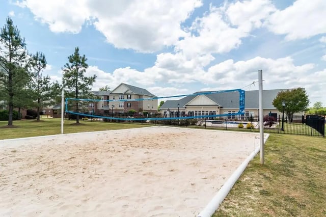 Sand volleyball court with net and apartment buildings exterior at Gamecock Village in Jacksonville Student Accommodation