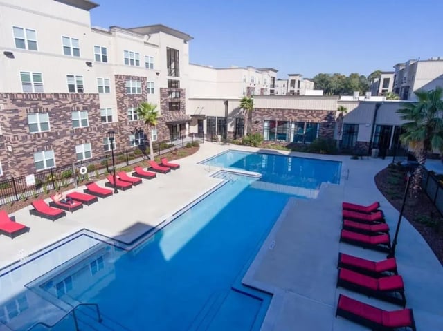 Apartment complex with L-shaped pool red lounge chairs exterior at Varsity House Gainesville in Gainesville Student Accommodation