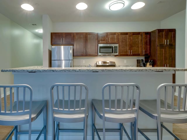 Bar stools at kitchen counter with cabinets and fridge at College and Crown in New Haven Student Accommodation