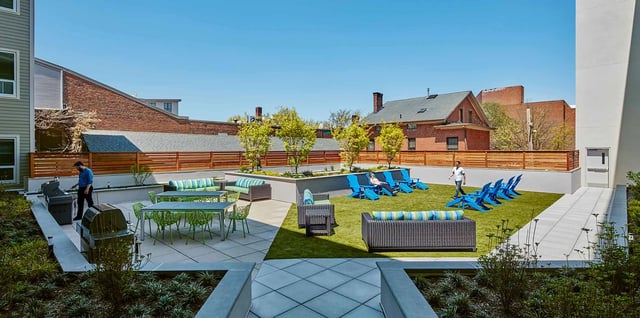 Patio with grills tables chairs couches and green lawn exterior at College and Crown in New Haven Student Accommodation
