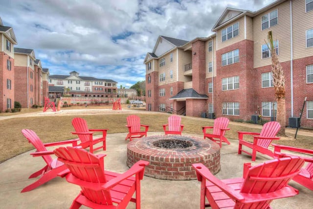 Red chairs surround brick fire pit outdoors patio area at Grove at Auburn in Auburn Student Accommodation
