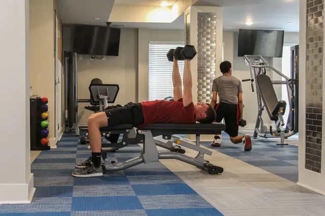Man on bench press with another man exercising gym area at Douglas Heights in Chattanooga Student Accommodation