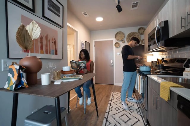 Woman reading at table man cooking kitchen at Summit Place in Charleston Student Accommodation