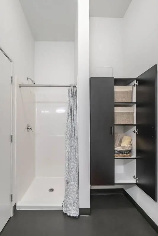 Shower stall with curtain and open cabinet with storage bathroom at Arena District in Eugene Student Accommodation