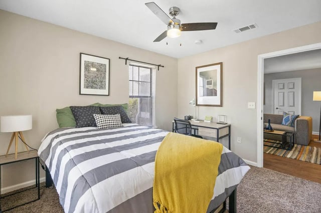Bed with striped comforter desk and adjacent living area bedroom at The Wilde Raleigh in Raleigh Student Accommodation