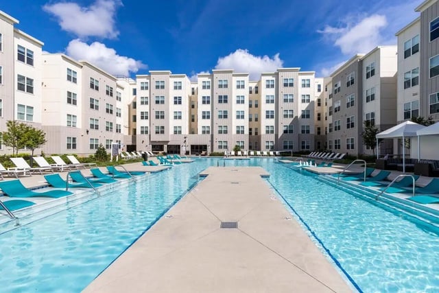 Apartment buildings surround a long swimming pool with lounge chairs exterior at Rush Charlotte in Charlotte Student Accommodation