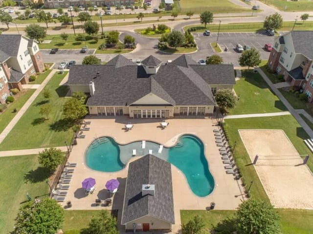 Pool lounge chairs umbrellas volleyball court exterior at Grove at Stephenville in Stephenville Student Accommodation