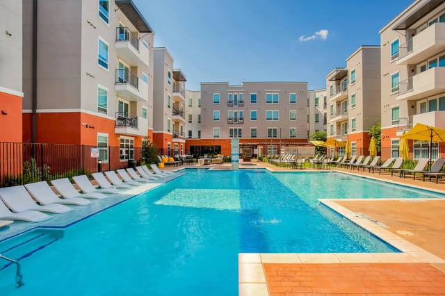 Apartment complex with pool lounge chairs and umbrellas exterior at Liv+ Arlington in Arlington Student Accommodation