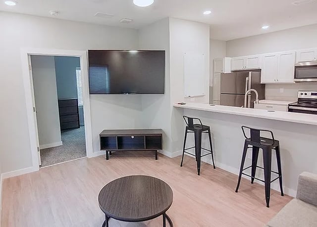Living room kitchen with bar stools and TV. at Rhelm in Pensacola Student Accommodation