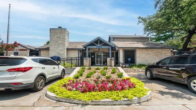 Stone building two cars flower bed exterior at Ironhorse Flats in Austin Student Accommodation