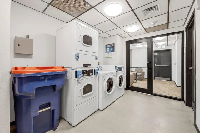 Stacked washers dryers blue trash bin Laundry room at Vista in Denver Student Accommodation