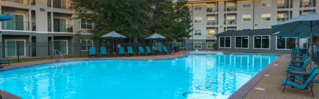 Blue lounge chairs and umbrellas by pool exterior at Regency Gardens in Bryan Student Accommodation
