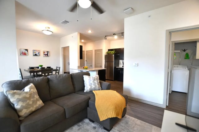 Gray sectional couch yellow throw dining table living room at Riverside Villas in Fort Worth Student Accommodation