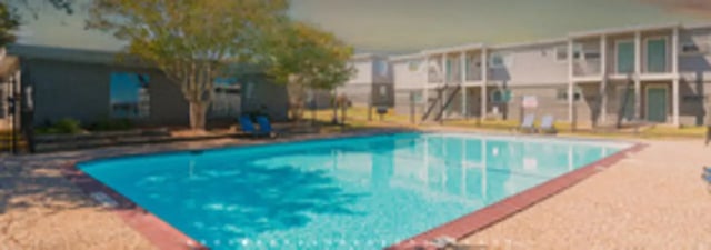 Swimming pool with lounge chairs and apartments exterior at The Grand 1501 in College Station Student Accommodation