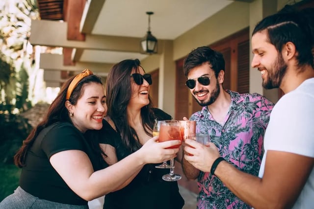 Four friends holding drinks toasting exterior living area at The Mercury in Austin Student Accommodation
