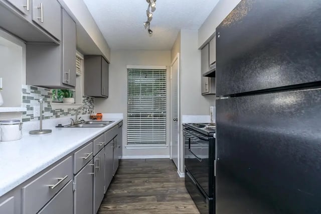 Grey cabinets sink stove refrigerator blinds kitchen at Villas at Shadow Oaks in Austin Student Accommodation