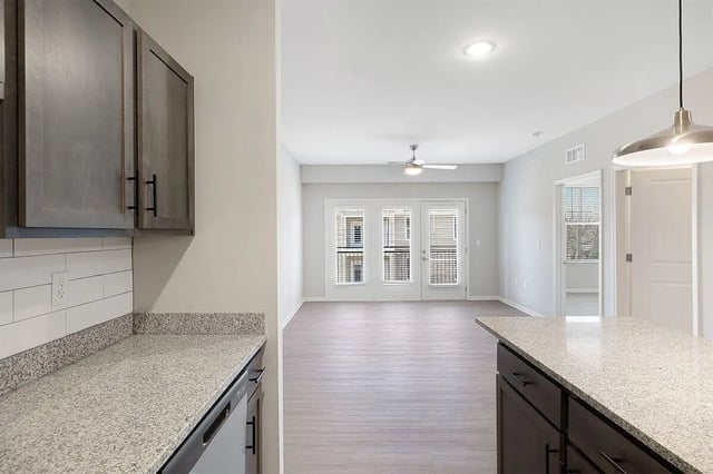Kitchen island cabinets with white tile backsplash and living area at The Belltower in Louisville Student Accommodation