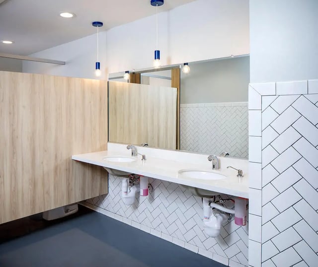 Two sinks mirror wood stalls tile wall bathroom at M @ College in San Diego Student Accommodation