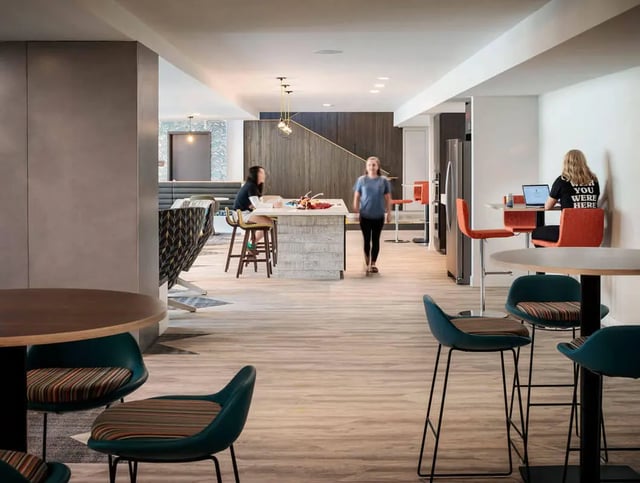 Students working at tables and walking communal living room at M @ College in San Diego Student Accommodation