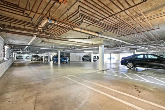 Cars parked in concrete garage with pipes overhead parking garage at Valleywood in Los Angeles Student Accommodation