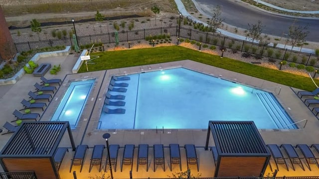 Lounge chairs surrounding illuminated pool and fire pit outdoor area at Claro at High Point in Aurora Student Accommodation