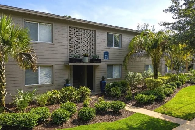 Tan building with palm trees and greenery exterior at Newport Square Apartments in Colorado Springs Student Accommodation