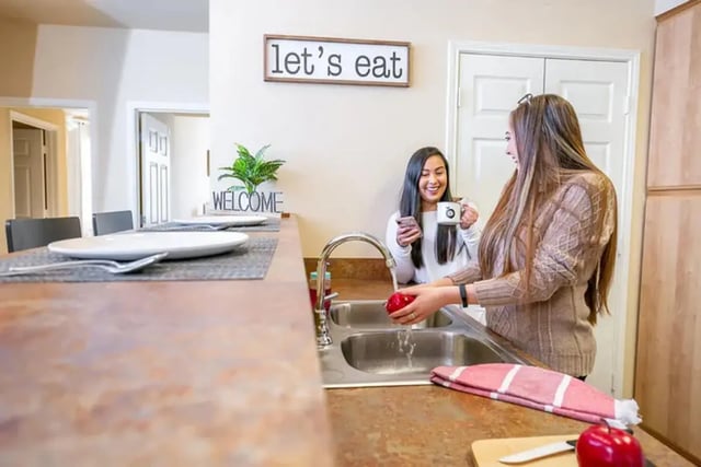 Two women washing an apple and holding a mug kitchen at University Crossing Apartments Ruston in Ruston Student Accommodation