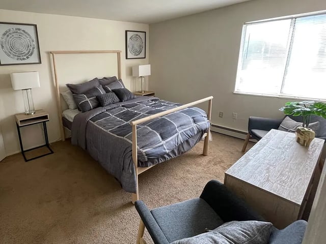 Bed with gray comforter two nightstands and two chairs bedroom at Breckenridge Apartments in Nampa Student Accommodation