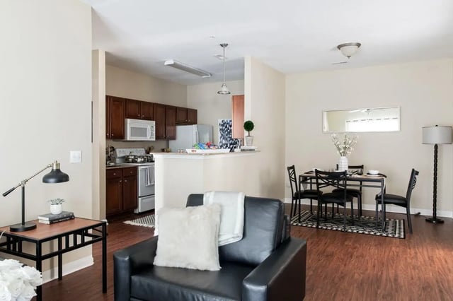 Black leather sofa with pillows dining table and kitchen living room at University Village at Greensboro in Greensboro Student Accommodation